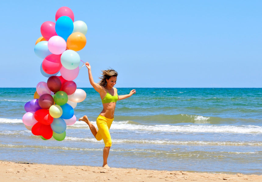 Donna che corre in spiaggia con palloncini colorati