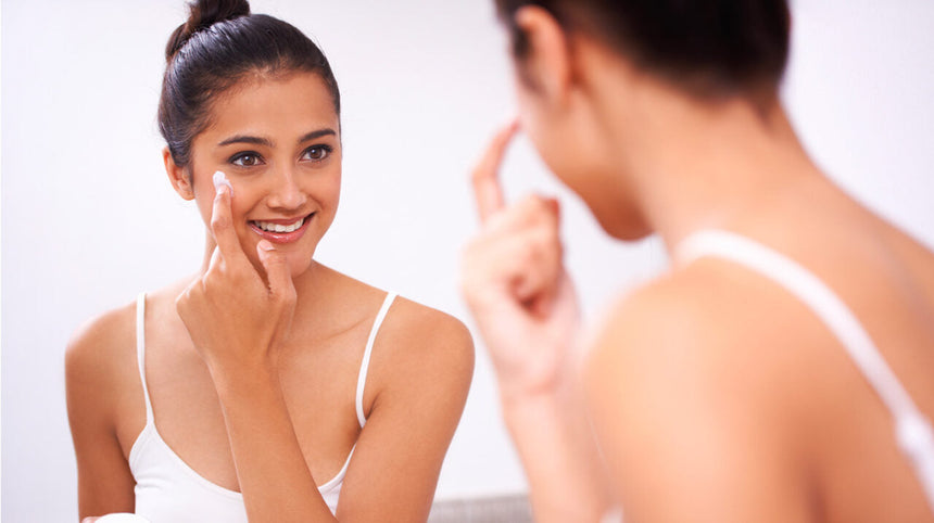 Ragazza che si applica una crema viso allo specchio