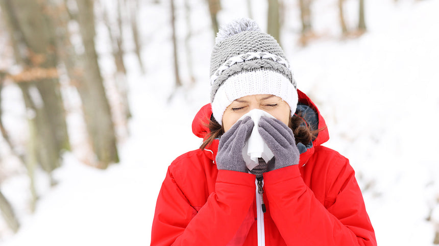 donna con giacca rossa che si soffia il naso in un bosco innevato