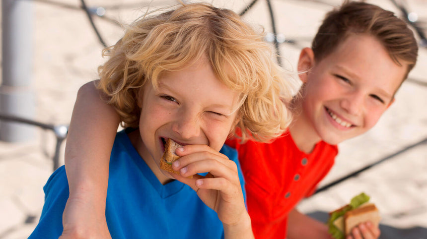 Due bambini che ridono mentre uno fa merenda